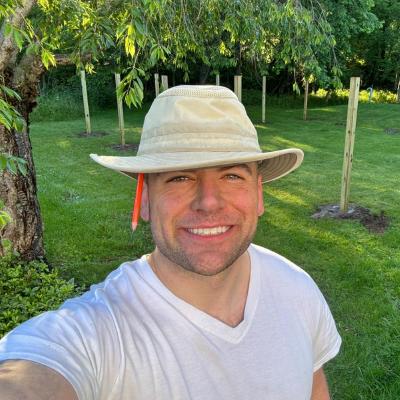 Joe Fusco smiling in a sun hat, in his garden among young trees